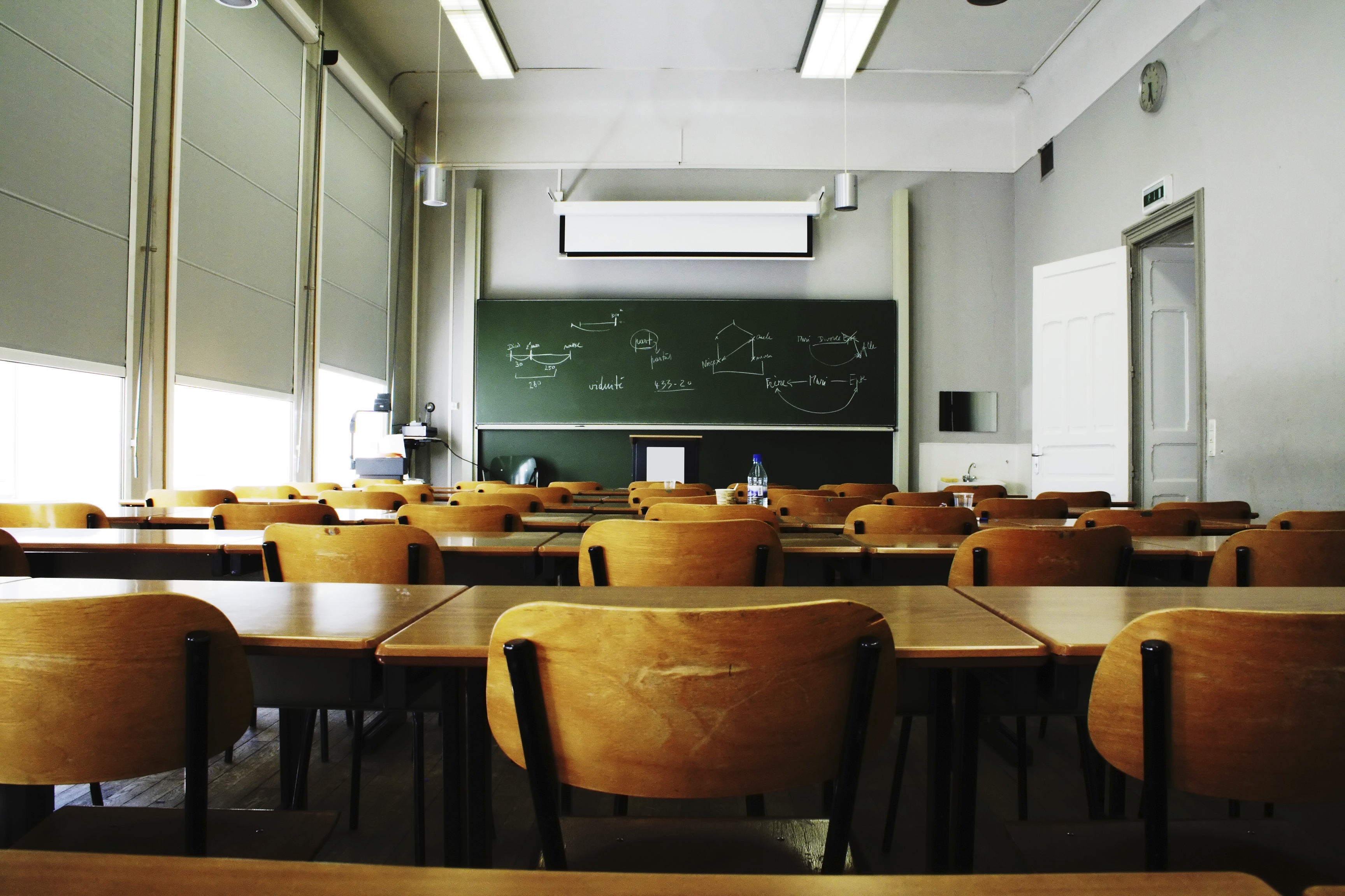 classroom with empty wooden chairs facing chalkboard