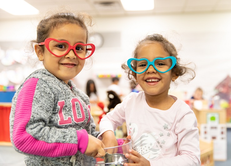 Two preschool children wearing colorful heart glasses and smiling