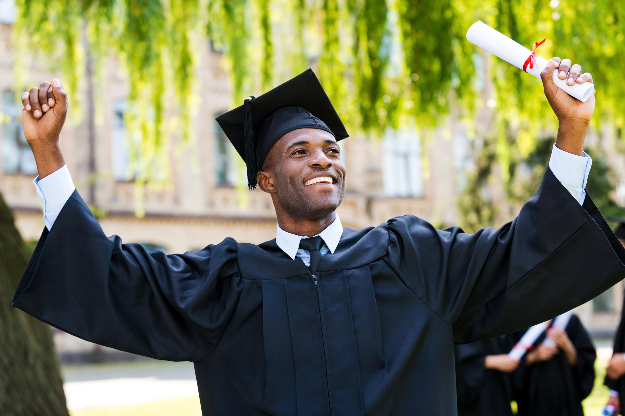 Man in graduation cap and gown raising up his diploma