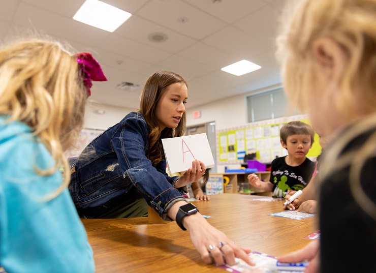 Teacher holding a paper with the red letter "A" teaches preschool students